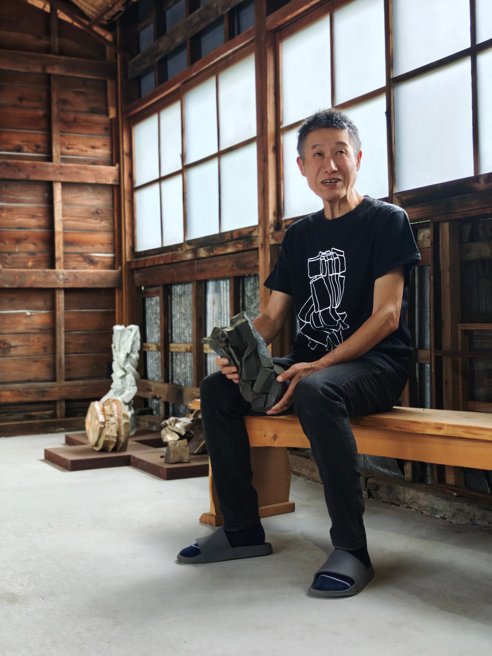 Shozo Michikawa seated in his Sasama studio holding a ceramic work