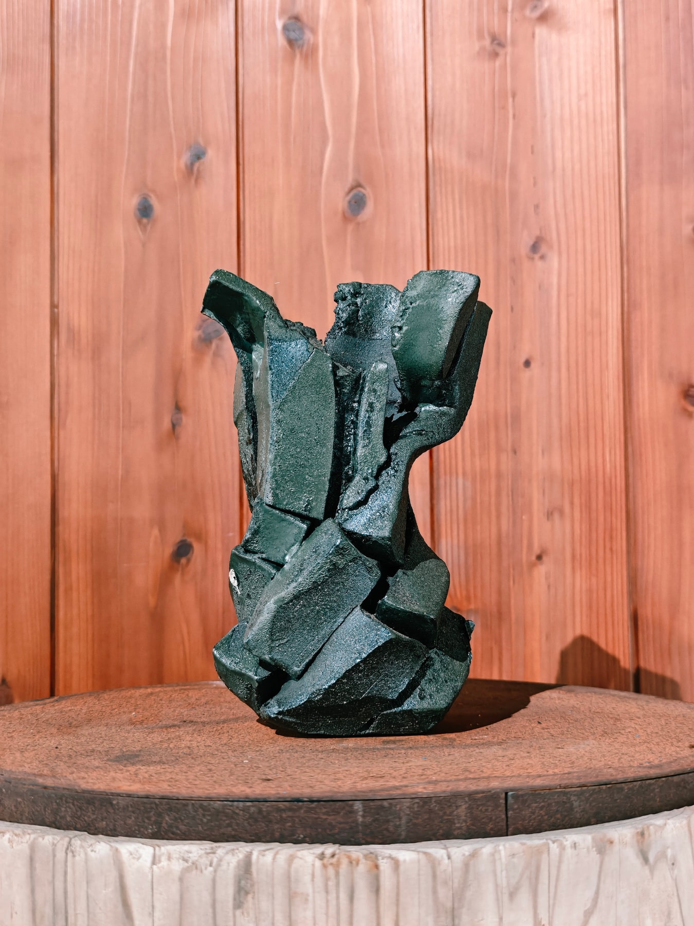 Dark sculptural ceramic work against a warm wooden wall